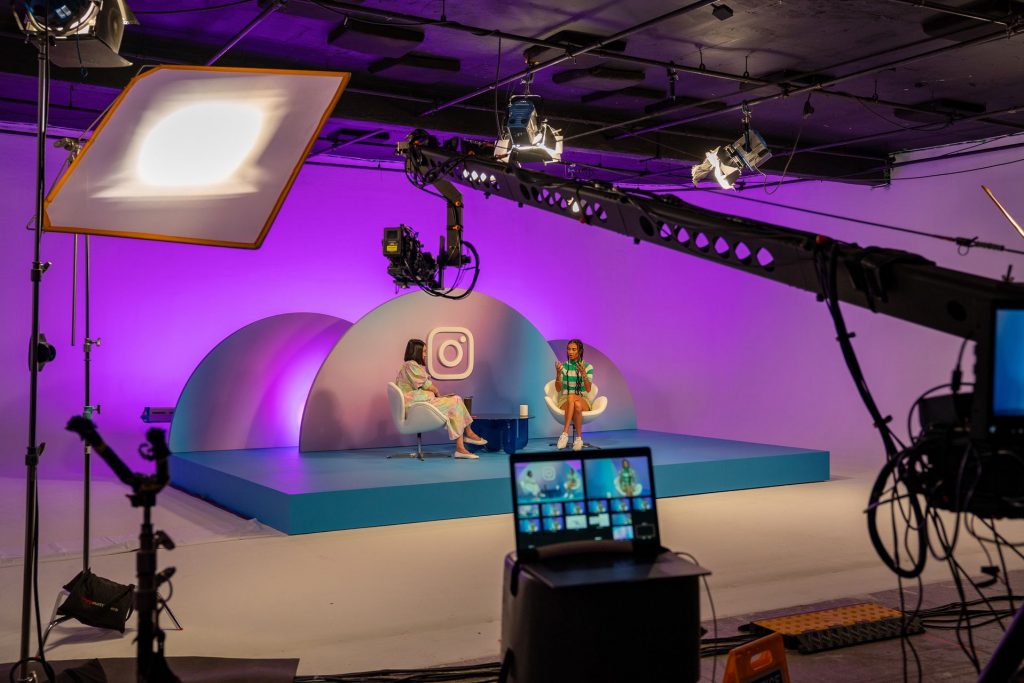A stage with two women sitting being filmed by a camera