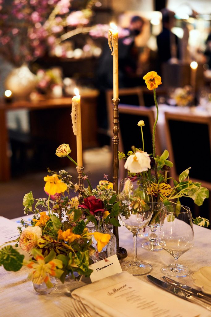 Wild baroque flower arrangement with tall lit candles on a white tablecloth table 